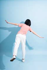 Asian individual performing a playful dance pose against a light blue backdrop with arms extended...