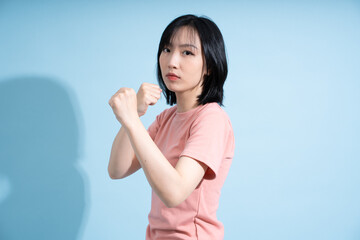 Confident Asian woman poses with fists raised against a light blue background during a portrait...