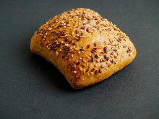 One small roll with grain and seeds on dark background. Fine bakery product made from high quality...