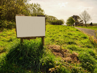 Small blank sign on a grass in a park. Warm sunny day. Informational billboard. Advertisement banner in rural country area.
