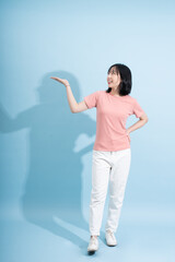 Young Asian woman poses against light blue background while smiling and gesturing with her hand in...