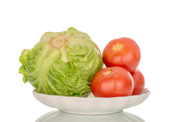 One fresh cabbage and three tomatoes on a white ceramic plate, close-up, isolated on a white background.
