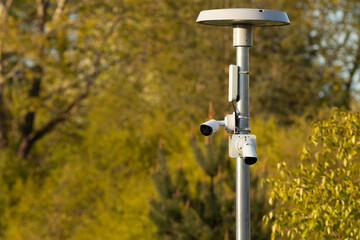 Two white surveillance cameras mounted on a metal pole with a circular antenna, set against a...