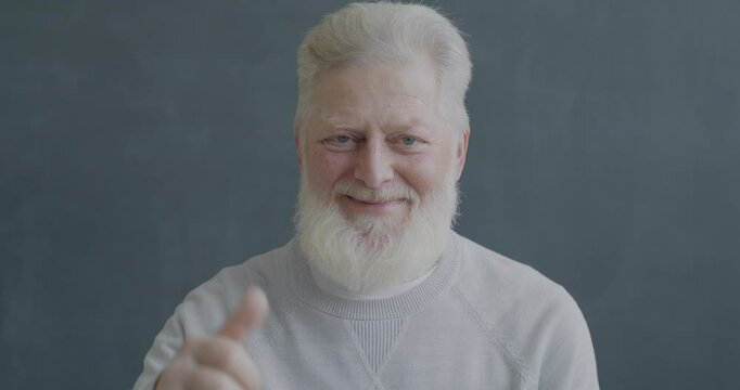 Slow motion portrait of pleased senior man showing thumbs-up hand gesture smiling looking at camera on black color background.
