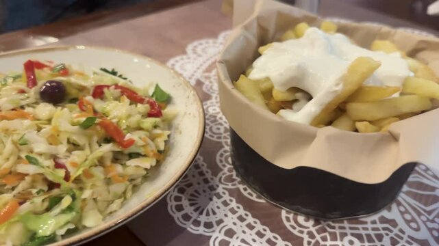 
Enjoy a serving of crispy fries topped with creamy sauce alongside a refreshing Greek gabbage salad named politiki at a cozy local eatery in the evening.