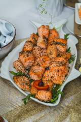 Close-up of grilled or oven-roasted salmon fillet pieces, seasoned with herbs and spices, served on a decorative white fish-shaped plate with fresh arugula. 