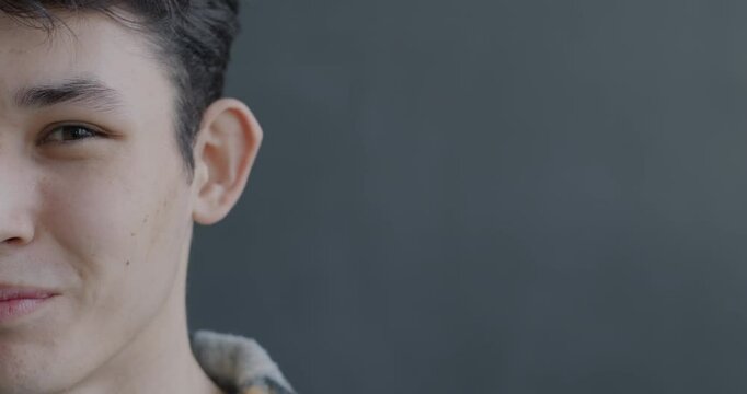 Close-up portrait of joyful Asian man half face laughing looking at camera on gray color background. People and good mood concept.