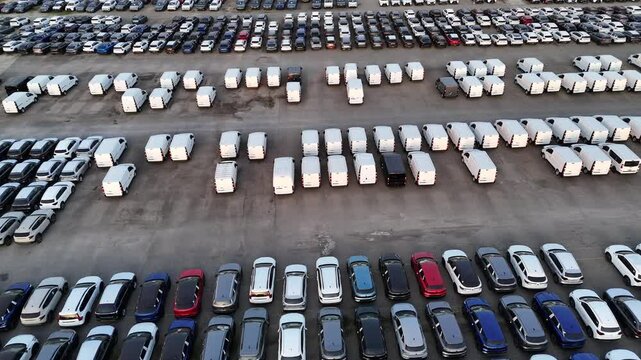 Drone captures an orderly car deposit with hundreds of vehicles and vans arranged in rows, part of a logistics hub for regional distribution, likely at an industrial site, slow motion
