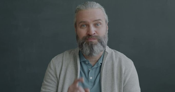 Slow motion portrait of pensive mature man thinking then raising finger having great idea smiling looking at camera on black color background