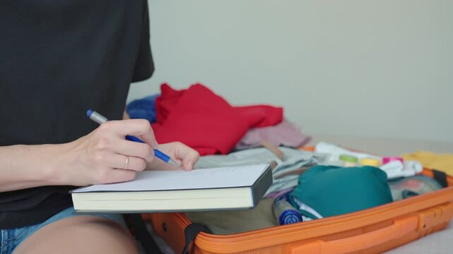 Woman preparing for travel, packing suitcase with clothes and checking travel packing list. Concept of holiday and vacation planning