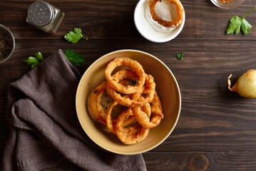 Crispy fried onion rings in bowl on wooden table