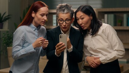 Happy excited women colleagues team group holding mobile phone multinational read good news businesswomen winning online finance celebrating office success offer ladies bet multiracial business people