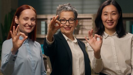 Three multiethnic businesswomen co-workers Caucasian Asian team women recommend females showing gesture ok okay smiling colleagues office approval support symbol business diversity multiracial ladies