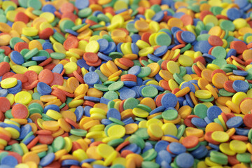 Bright multi-coloured background. Lots of multi-coloured sugar round pucks. Culinary sprinkles