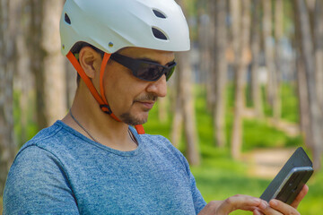 Short Respite: A sport enthusiast paused their bicycle ride to check data on a phone screen amidst the pine trees of an urban park. Photo as part of a series that highlights theme of healthy living.