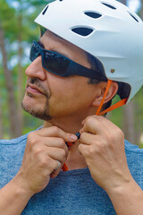 Preparation to Cycling: A portrait of a sport enthusiast fastening strap of a bicycle helmet against the background of an urban park. Photo is part of a series that highlights theme of healthy living.