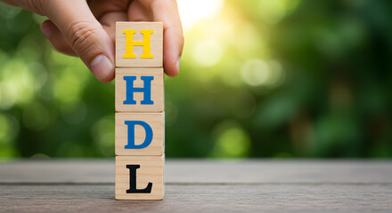 Hand Stacking Wooden Blocks Spelling HDL Against Blurred Green Background with Sunlight