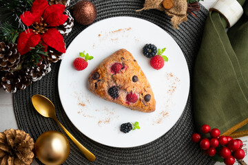 Triangular English scones with blackberries, raspberries and chocolate chips. Top view table with christmas decorations.