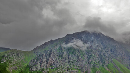 small cloud in front of rock mountain under grey sky