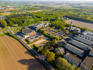 Aerial view of a rural area with a large building complex surrounded by farmland, green forests, a...