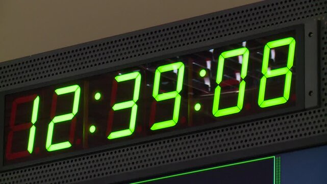 Close-up of a large digital clock with bright green LED numbers. Seconds visibly count upwards, showing the precise passage of time on an electronic timer display.