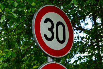 Znak drogowy informujący o ograniczeniu prędkości do 30 km/h (B-33), ustawiony przy drodze. Okrągły znak z białym tłem i czerwoną obwódką to typowy znak ostrzegawczo-nakazowy stosowany w strefach. 