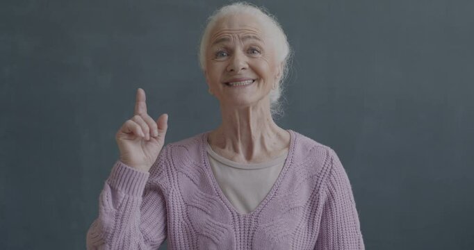 Slow motion portrait of happy senior lady raising finger having brilliant idea on black color background. People and problem solving concept.