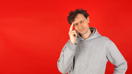 unhappy, angry, agonized curly man in gray hoodie massaging temples bridge nose, suffering from...