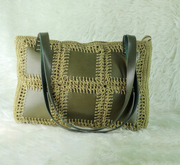 Green shoulder bag knitted using faux leather pieces on a white fluffy blanket. Close-up. Bag crocheted with square motifs. 