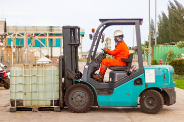 Forklift operator in safety uniform moving large IBC container at outdoor industrial facility.