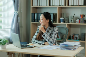 Obraz premium Professional female accountant reviewing annual expense reports at her desk with a laptop and paperwork — ideal for finance, tax, and corporate business themes.
