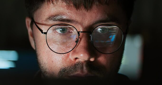 White Caucasian male software developer work late night, program coding in home office. Computer engineering job, data scientist, cybersecurity, information technology. Close-up eyeglasses, handheld