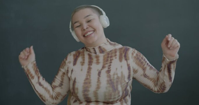 Slow motion portrait of young Asian woman listening to music with headphones dancing having fun on black background. People and entertainment concept.