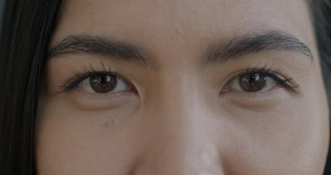 Close-up slow motion portrait of Asian woman's eyes looking at camera blinking with no emotion. People and human body part concept.