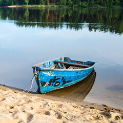 Obraz premium Rustic blue rowboat resting on a sandy shore, reflecting in calm water. Evokes peace, tranquility, and escape. Ideal for travel, nature, or reflective themes.