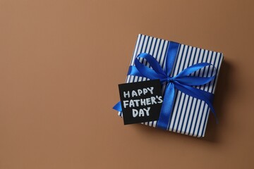 Father's Day concept. Top view photo of giftbox with silk ribbon bow on brown background