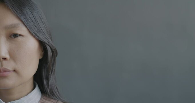 Close-up portrait of young Asian woman half face looking at camera with no emotion on black color background. People and expression concept.