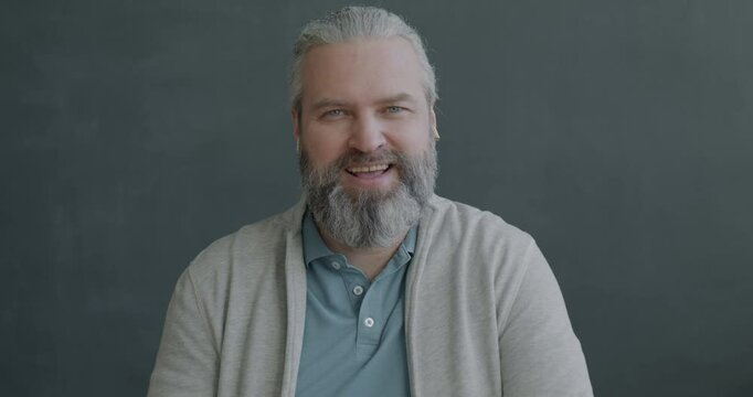 Portrait of mature man making online video call speaking showing OK gesture using earphones on gray color background. People and communication concept.