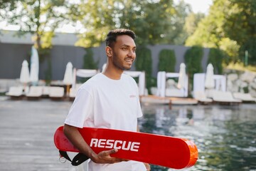 Lifeguard holding rescue equipment smiling at poolside