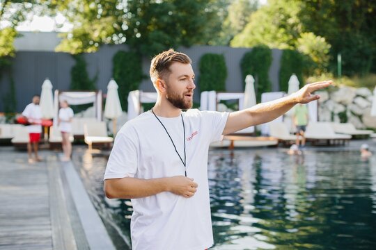 Lifeguard gesturing and supervising swimmers at the poolside