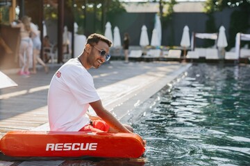 Lifeguard sitting by the pool with rescue equipment, ensuring safety