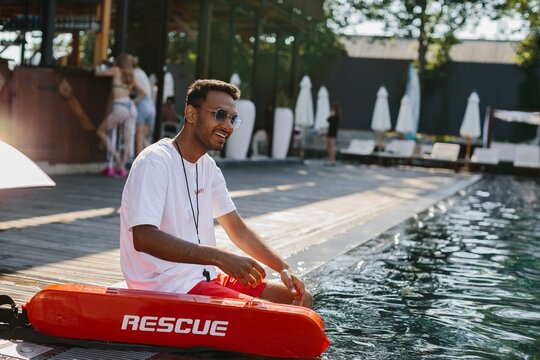 Lifeguard sitting by the pool with rescue equipment, ensuring safety