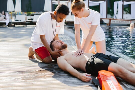 Lifeguards performing cpr on unconscious swimmer by poolside