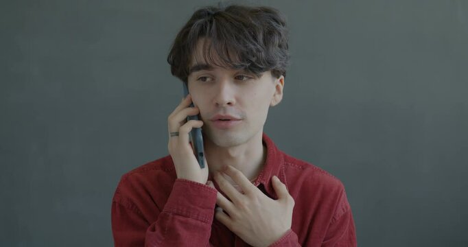 Portrait of young man speaking on mobile phone smiling holding gadget on black background. Cellphone communication and people concept.