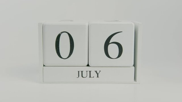 A hand flips a wooden calendar from July 6th to July 7th on a white background, illustrating the passage of time