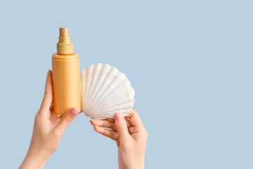 Female hands with seashell and sunscreen cream on blue background