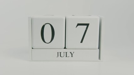 A hand flips a wooden calendar from July 7th to July 8th on a white background, marking the transition of time