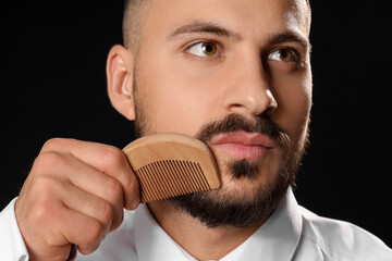 Handsome young bearded man with comb on black background