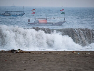 Naklejka premium Fishermen are forced to go to sea to look for fish amidst very large waves on the southern coast of Java due to changes in the earth's climate.