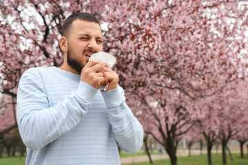 Sick young man with tissue suffering from allergy outdoors